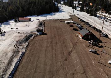 A large, dry, and cleanly plowed parking lot with a small building, next to a sled hill and ski trail with deep snow.