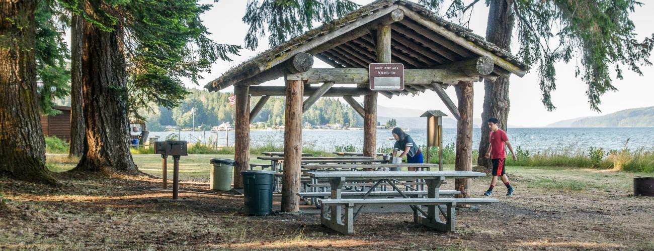 round log picnic shelter with tables , bbq grill and trash cans 