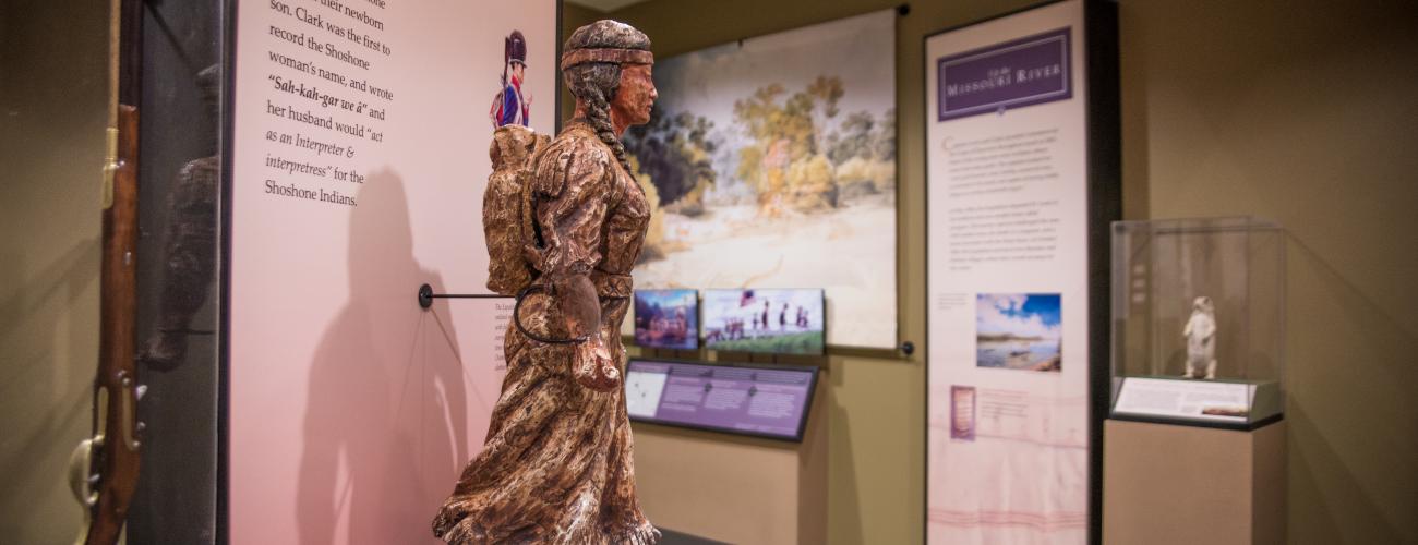 Inside the Interpretive Center, a small statue of Sacajawea sits on a podium with a narrative of the history of the Lewis and Clark Trail journey behind her. Other displays can be seen in the background.