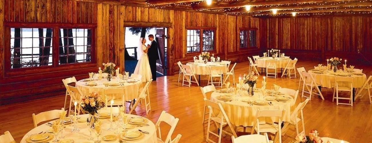 A couple stands by the door of a log cabin with the interior set for a wedding in golden light.