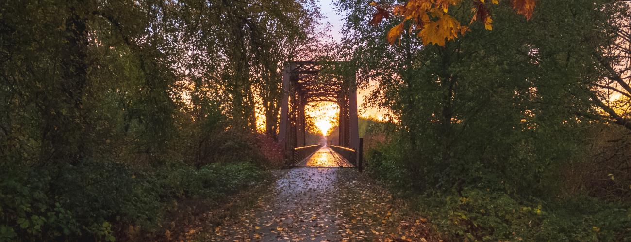 A trail running through an old railroad bridge surrounded by brilliant fall foliage and a spectacular gold, pink and blue sunset. 