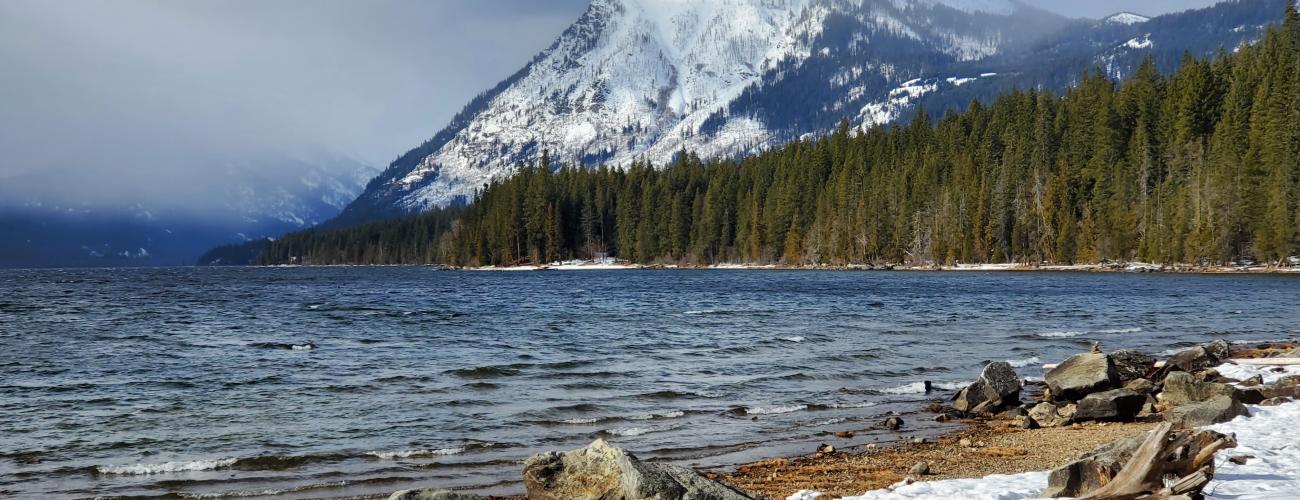 snow covered mountains in background above lake with snowy beach