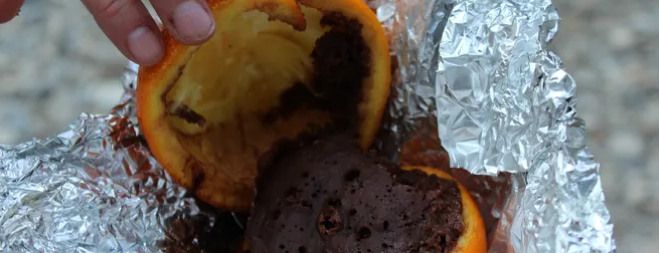 A halfed orange in tin foil. The orange top of the orange is pulled back and there's chocolate cake inside the rind.