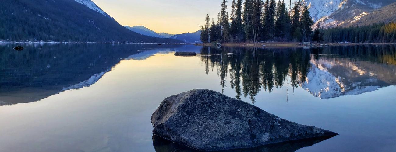 A lake and mountains with rock in foreground at sunrise.