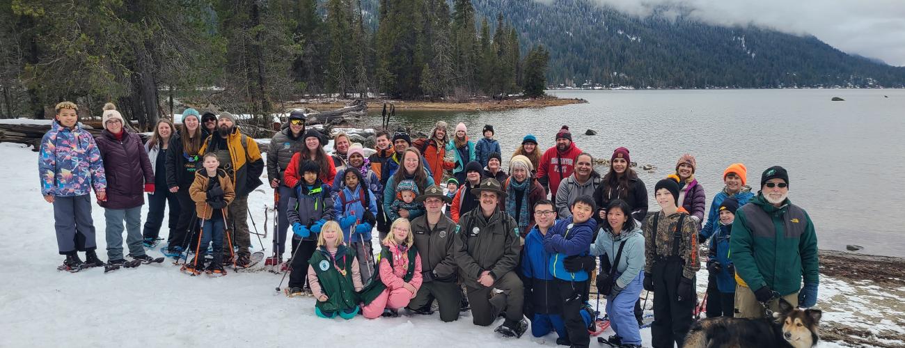 Large group of hikers standing in snow, in front of Lake Wenatchee