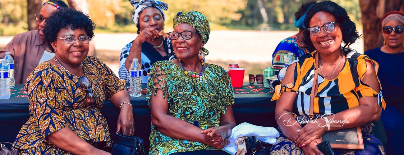 Some African American women and men dressed in colorful clothing and sitting at a picnic table in a park