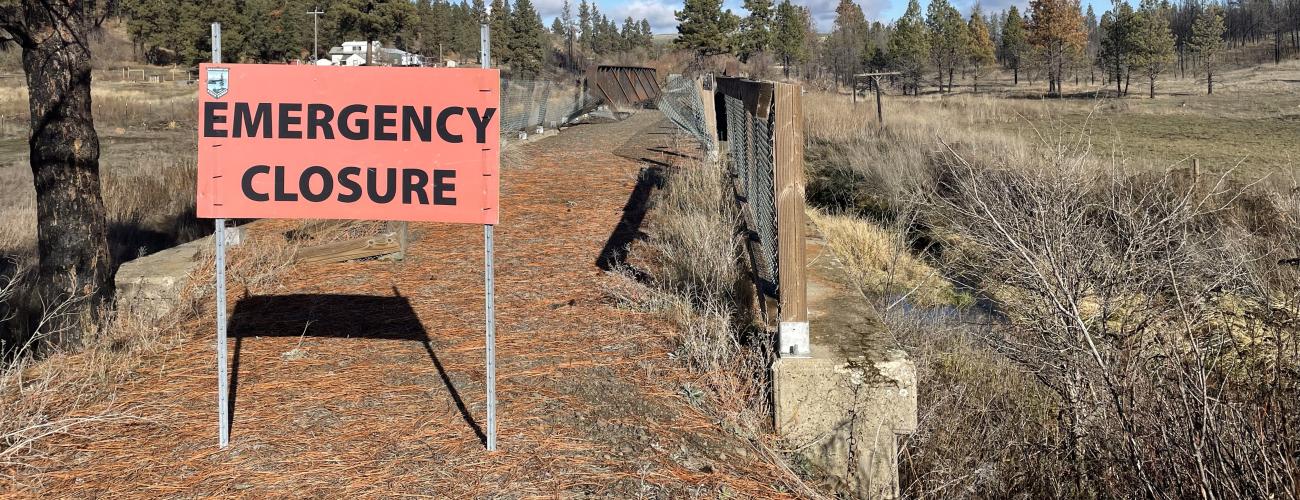 An emergency closure sign in front of a bridge that has been burned in a fire.