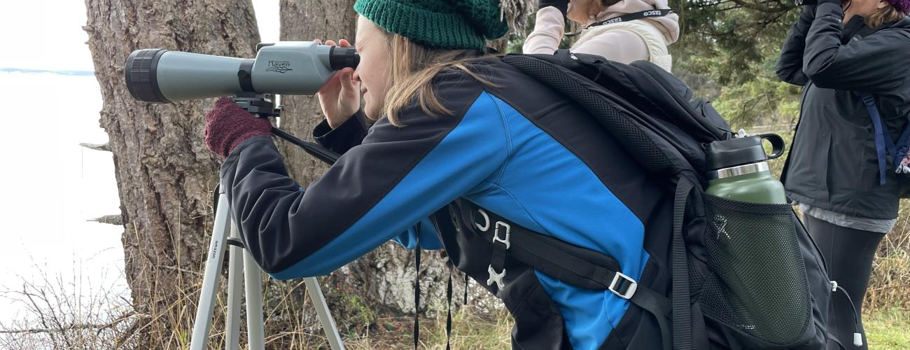 Person wearing blue and black jacket looks through spotting scope as they look for birds