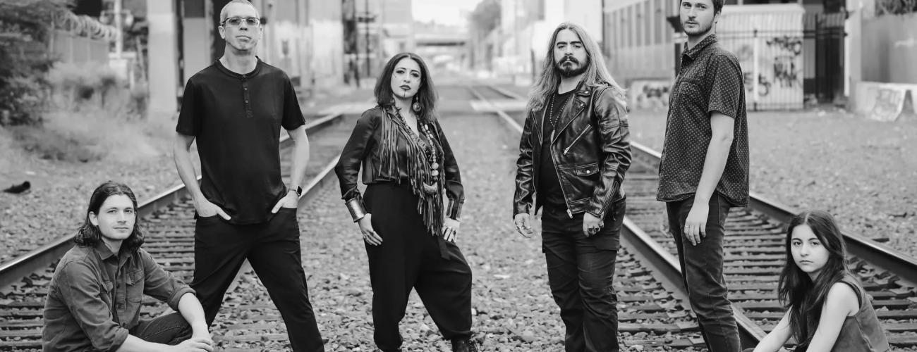 A group of 6 musicians standing between 2 railways in an urban setting, black and white picture