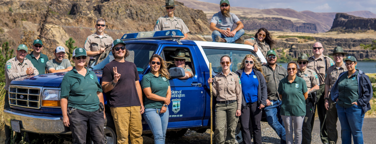 A group of staff around a ranger truck with brown bluffs in the background.