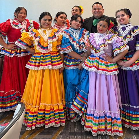 A group of dancers in colorful Mariachi costumes pose.