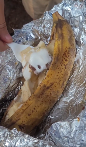 Spoon digs into banana stucked with chocolate and marshmallows