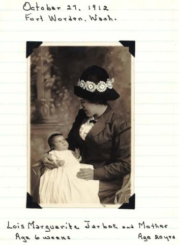 A sepia toned formal portrait of a woman holding and looking at an infant.