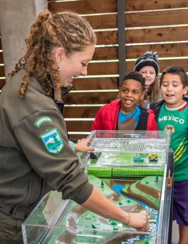 A woman in a Parks uniform shows children a diagram of a park.