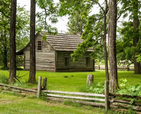 old world cabin of wood surrounded by green grass and wood rail fence