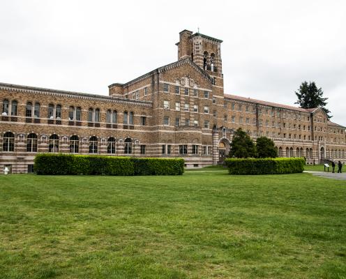The Seminary at Saint Edward State Park where the Saint Edward Lodge can be found. The building is very long with a center building that appears to be 2 floors higher than the rest of the building. There is also a bell tower that reaches above the tallest part of the building. The lawn area of the seminary is also visible with bright green grass and well manicured hedges, 