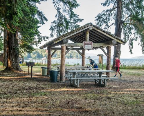 round log picnic shelter with tables , bbq grill and trash cans 