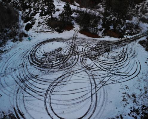 Circular parking area covered by a light layer of snow and looping tire tracks coming off a plowed highway.