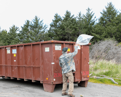 Person throwing away trash in a dumpster as they leave a park