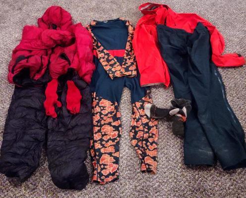 Three layers of red, green and black clothing: wool base layer (middle), warm down layer (left) plus wool gloves, and rain shell top and bottom.