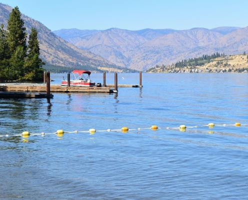 A lake with tan hills in the background and swim area cordoned off in the foreground.