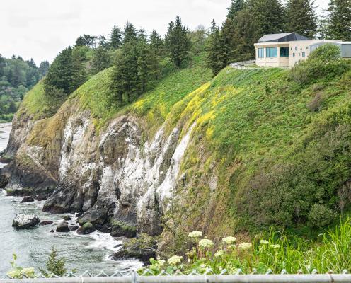 A building on the edge of a green cliff with ocean below.