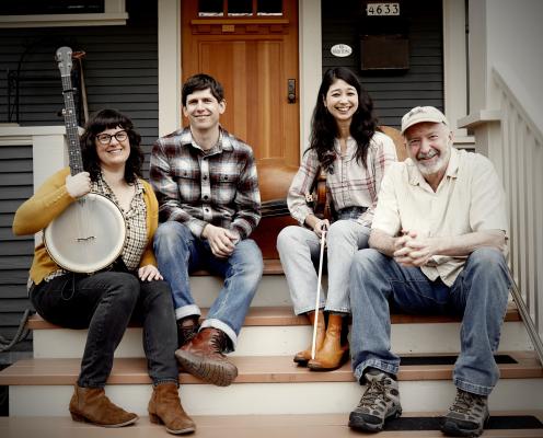 A group of four musicians sit on the steps of a house.