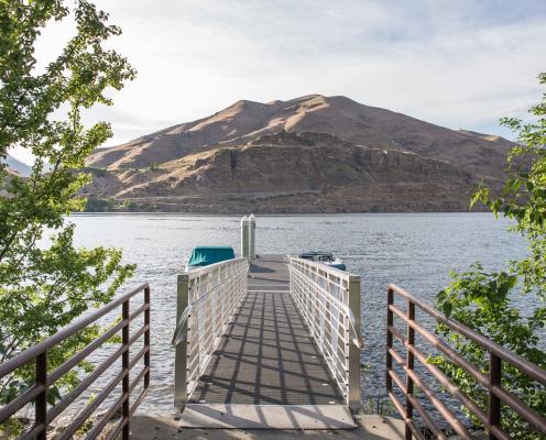 A dock surrounded by trees facing a hill across a river.