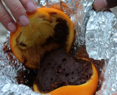 A halfed orange in tin foil. The orange top of the orange is pulled back and there's chocolate cake inside the rind.