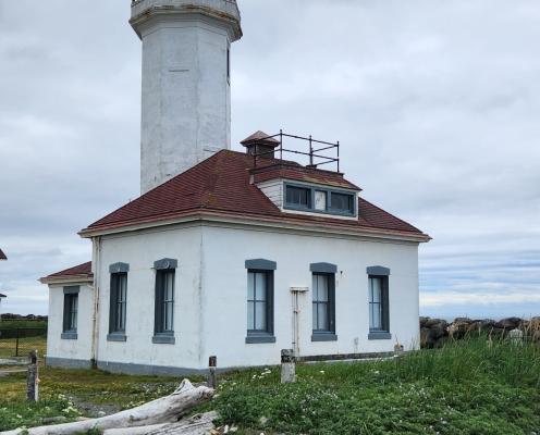 A view of Point Wilson Lighthouse at Fort Worden State Park. The lighthouse is white with a red roof right on the beach.