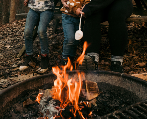 small campfire burning in one of our parks' fire pits with a mom and two kids roasting a marshmallow around the fire