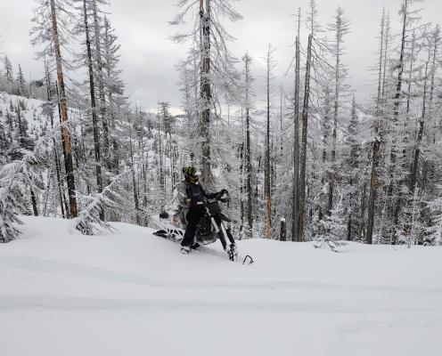 A snowmobiler on a flat snowy area with mountains behind.