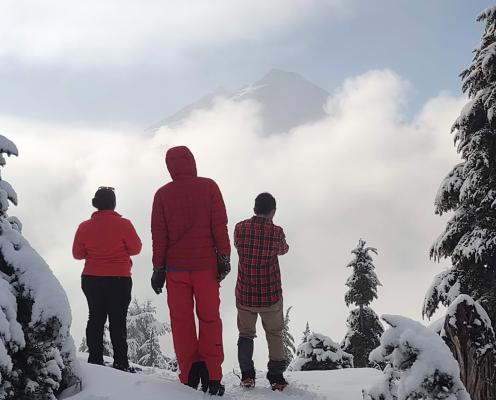 Mt Baker NRA Sno Park 3 people in red look at Mount Baker, shrouded in clouds