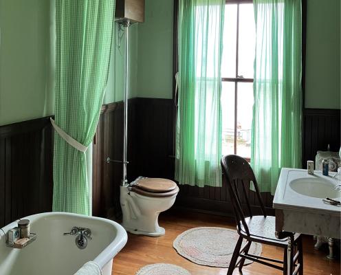 Green bathroom with white claw foot tub and sink in a historic home