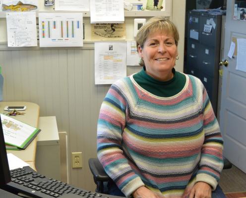 A woman in a sweater sits behind a computer in an office