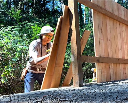 A woman with braids and tattoos builds a wood fence