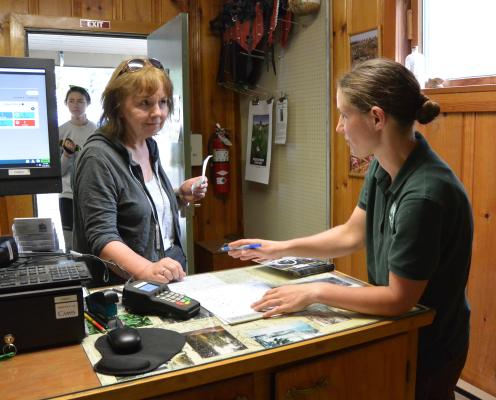 An office worker in a Parks shirt helps a customer while another customer waits in the doorway