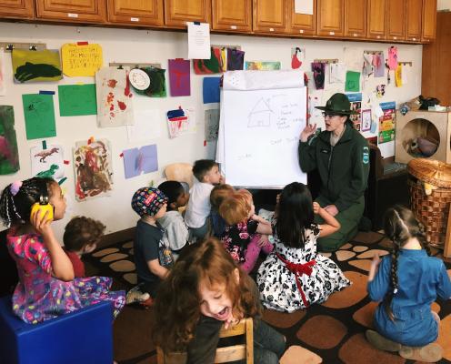 A woman in a park ranger uniform gives a presentation to a class of small children.