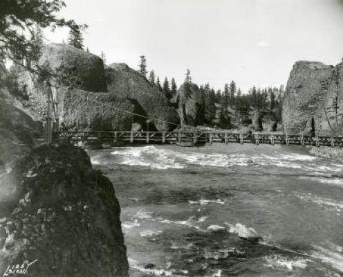 historic black and white photo of suspension bridge across rapid river surrounded by large basalt rock monoliths