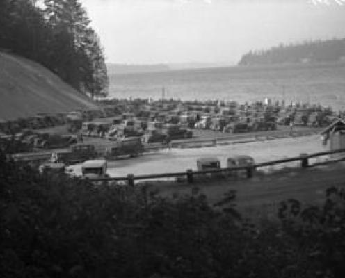 historic black and white photo of many cars parked in a parking lot close to a beach