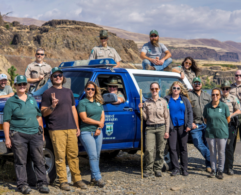 A group of staff around a ranger truck with brown bluffs in the background.