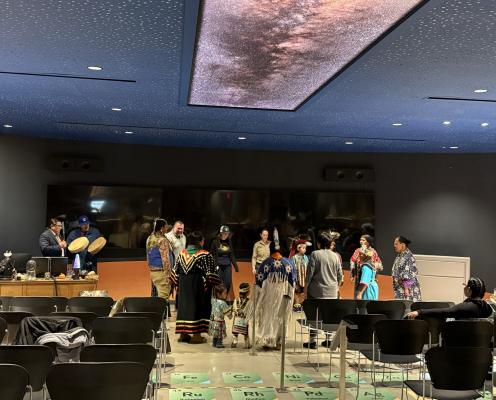 Adults and youth dressed in traditional Native American outfit dance in a circle in Goldendale Observatory 