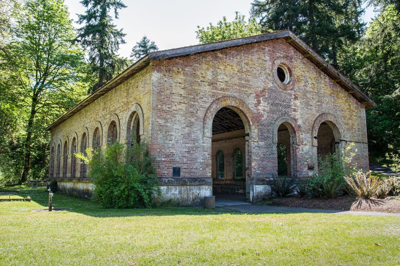a brick building stands on a lawn with open arch windows.