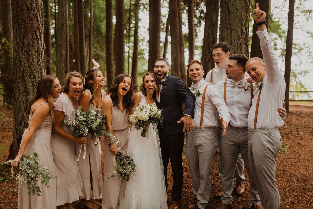 A bride and groom hug and smile while surrounded by their wedding party