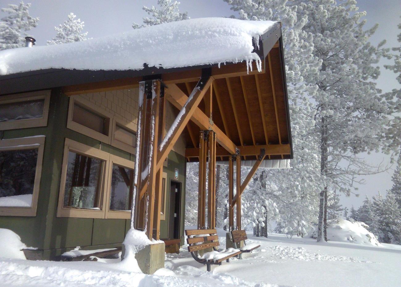 A snow-covered hut surroudned by snow-covered trees