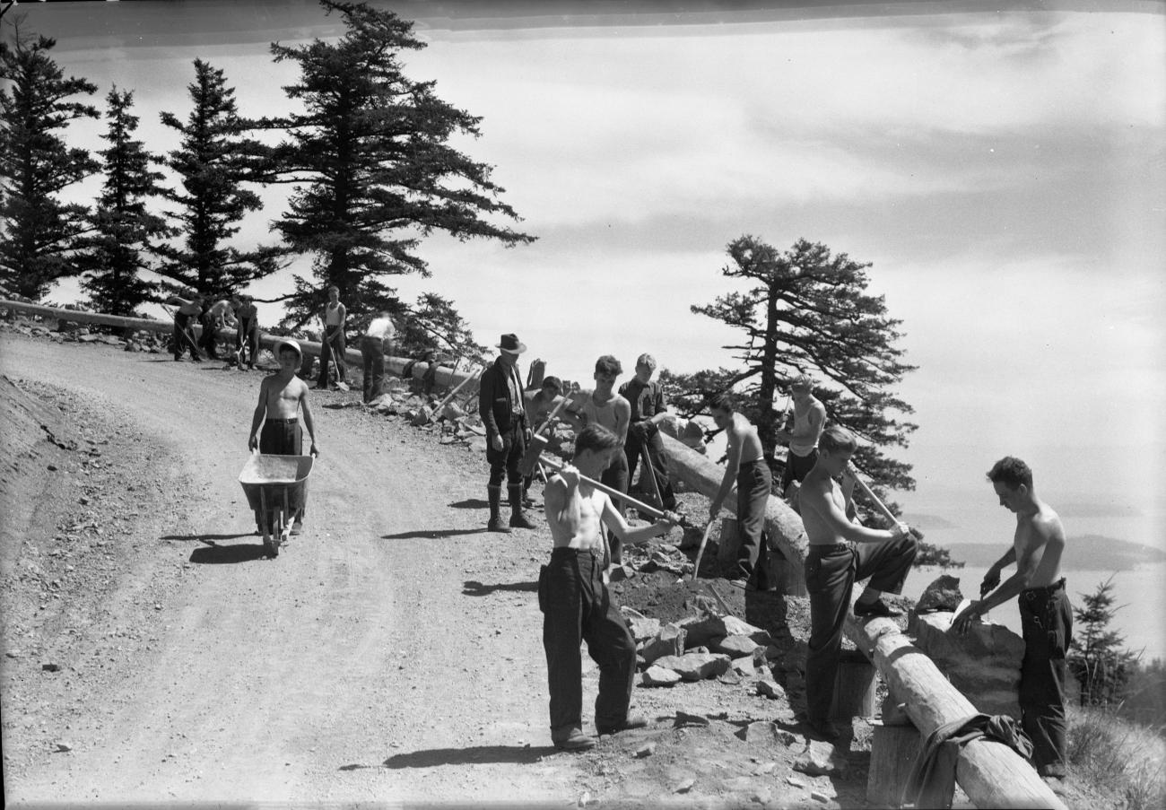 black and white historic photo of workers building guardrail at edge of exposed cliff