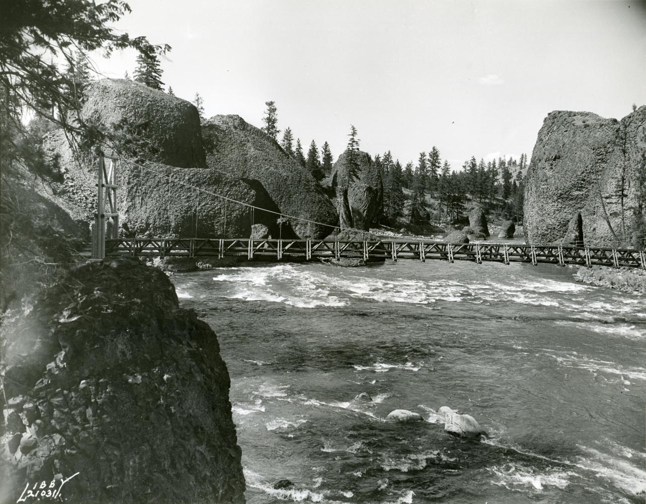 wooden suspension bridge over rushing river surrounded by dark rock cliffs