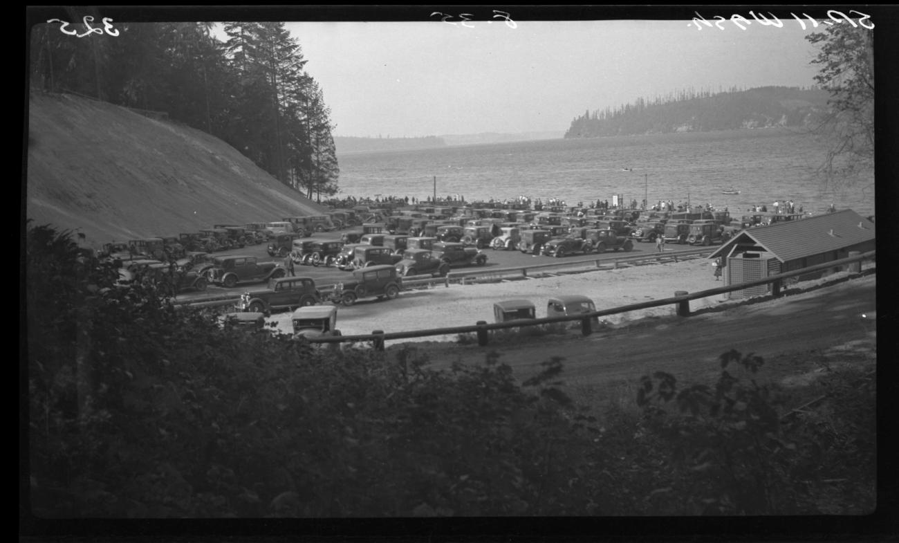 historic black and white photo of many 1930s era automobiles parked in parking lot near a beach