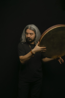 A man playing Iranian Daf, which is a Middle Eastern frame drum musical instrument, in black background.