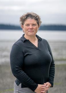 Washington State Parks Director Diana Dupuis stands on a rocky shoreline with ocean water and islands in the background. 